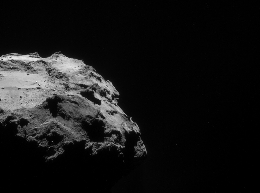 A close view of comet 67P/Churyumov–Gerasimenko: its sunlit limb filling the left of the frame, boulders and dust in sharp relief, the rest black space.